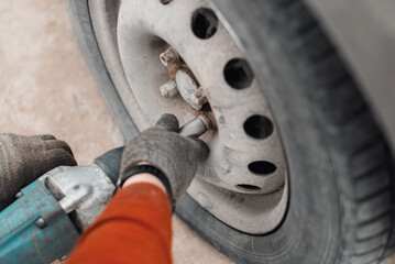 Mechanic repairing broken car or seasonal wheel replacement concept. Close-up of male hands using electric tool impact wrench outdoors. Selective focus.