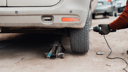 Car repair, problem, wheel replacement concept. Close-up of mechanic using an electric wrench repairing car on jack outdoors. Selective focus on wheel