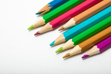 Fototapeta premium close up of vivid coloured pencils entering the left of the frame on a white background copy space from above