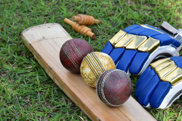 Old training cricket sport equipments on grass floor, leather ball, wooden wickets, gloves and wooden bat, soft and selective focus, traditional cricket sport lovers around the world concept.