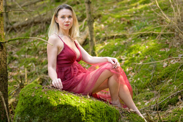Naklejka na ściany i meble Confident blond woman sitting on moss covered rock.