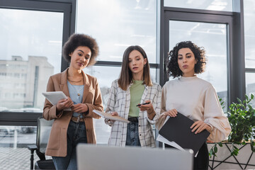 Obraz premium Multicultural businesswomen with notebook and papers looking at blurred laptop in office.