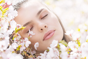 Obraz na płótnie Canvas Beauty, lifestyle and nature concept. Beautiful brunette woman portrait in white sakura blossom background during spring time in sunny day. Model placed head on blossoms with closed eyes and dreaming