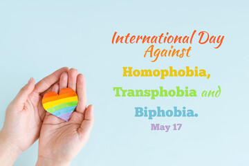 Concept International Day Against Homophobia, Transphobia and Biphobia. May 17. Stop Homophobia. Heart with rainbow LGBT flag in hands on blue background.