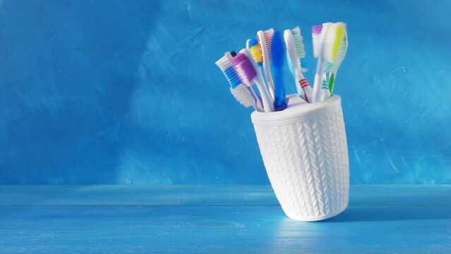Many different toothbrushes in a white cup swirl on a table against a blue background. 4k creative raw loop video. Filmed on high speed cinema camera, 1000fps.
