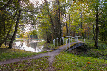 Narrow dirt path to an old bridge across a channel in a country autumn park. Alu Manor, Estonia.