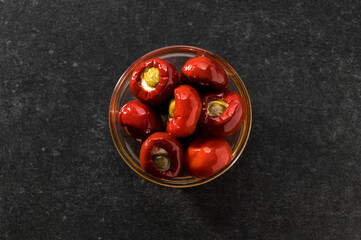 Red chilli stuffed with ricotta and capers in oil, top view, central composition, close-up, gray background