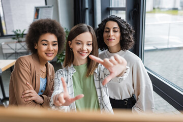 Cheerful interracial businesswomen looking at blurred board in office.