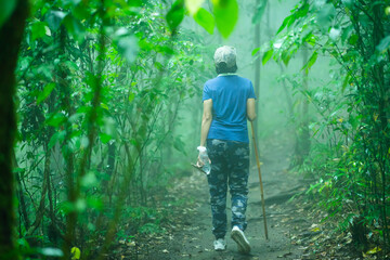 A young woman walks towards a large forest that is naturally lush with the pouring rain