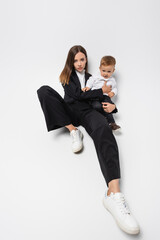 young woman in black suit sitting with little son on white.