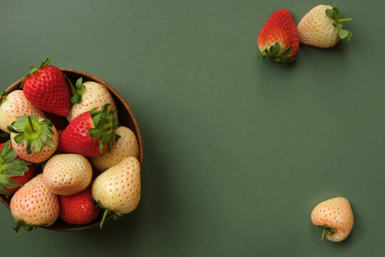 Close-up Of Pineberries (white And Pink Strawberries) And Red Strawberries In A Wooden Bowl On Green Table Shot From Above