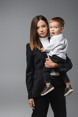 woman in black suit holding amazed son isolated on grey.