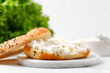 Bagel sandwich with cream cheese on marble board and white background.