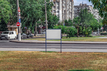 A white empty billboard stands on the lawn on a city street in Mykolaiv, Ukraine. Mockup of a steel signpost, outdoors