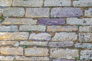 Texture of ancient stone paving stones close-up. Top view of old shabby colorful decorative blocks installed on the road