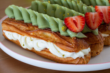 French eclairs filled with cream , garnished with pistachio cream and strawberries