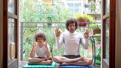 father and 7-year-old son boy do yoga relaxing exercises at home in the balcony with the arrival of spring they get ready for summer - meditation outside of the window