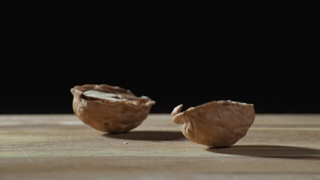 A whole walnut falls on a wooden kitchen cutting board on a black background and splits into two halves.   Slow motion and macro.
