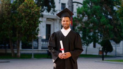 Good looking guy in his graduation day wearing a suit and graduation cap and posing in front of the...
