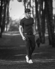 Full body portrait of handsome young man in forest environment, black and white image.