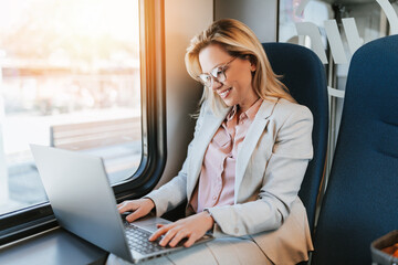 A middle-aged business woman is sitting in the cab of a high-speed train and working on a laptop.