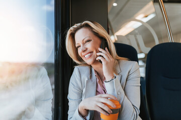 A middle-aged business woman is sitting in the cab of a high-speed train, looking through window and talking on phone.