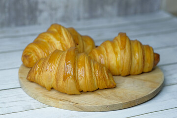 Fresh baked croissants on wooden cutting board on concrete grey surface in dark 