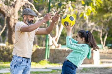 Mature indian father and young daughter playing soccer or football together in the summer park outdoor. man enjoying games and sports activity with girl kid.