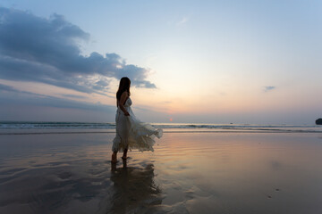Happy Woman wearing white dress enjoying the beautiful sunset on the beach