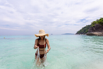 woman wearing a straw hat and orange bikini relax on the beach with beautiful blue sky.at Similan island Phuket Thailand , summer vacation concept
