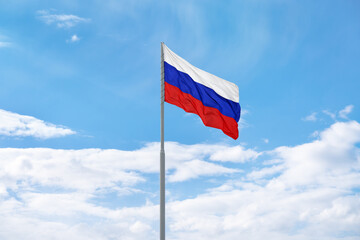 Russian white-blue-red flag is waving in front of blue sky and clouds