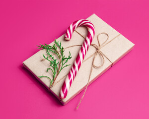 Gift wrapped in craft paper and candy cane on pink background. New Year or Christmas concept.