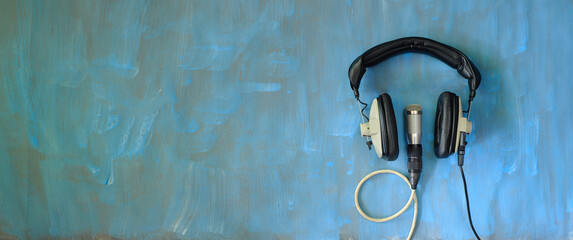 Podcasting concept, vintage headphones and recording microphone on grungy blue background, negative technique.