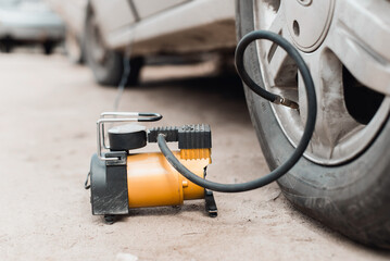 Wheel repair, pumping air into tire with car compressor outdoors. Close-up, low angle view, selective focus on electric pump - obrazy, fototapety, plakaty