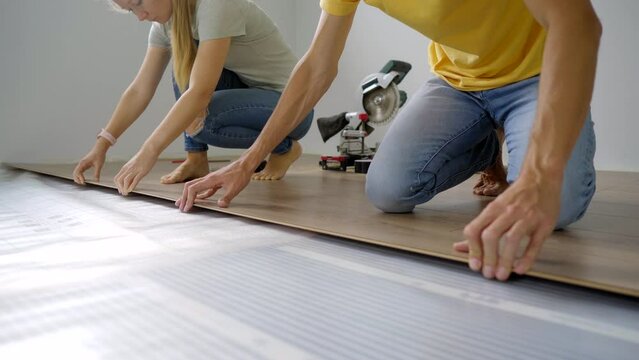 A family of woman and man install laminate on the floor in their apartment. DIY concept