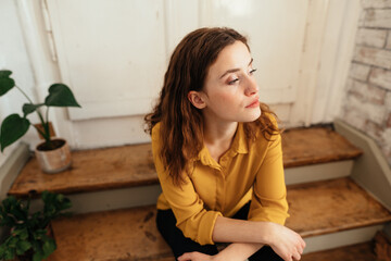 Young woman looks thoughtfully to the side and sits on an old staircase