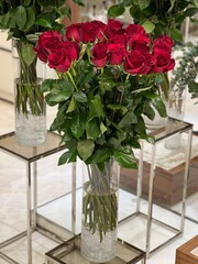 Stylish interior composition with a bouquet of red roses. tall Gorgeous red roses in a transparent glass vase on a glass table. Phytodesign in the interior of a store, salon or studio.