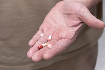 tablets in capsules and halves of tablets in the male hand of an elderly man. Concept: take pills and medications.