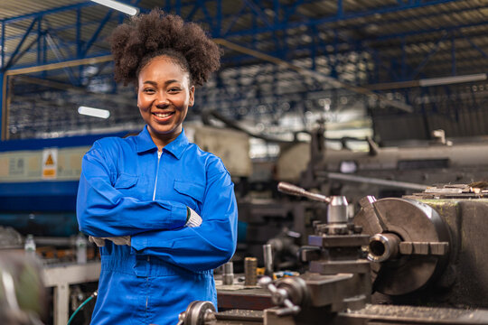 African American Young woman worker  in protective uniform operating machine at factory Industrial.People working in industry.Portrait of Female  Engineer looking camera  at work place.