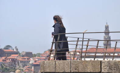 Obraz premium Pessoa do sexo feminino num miradouro da cidade do Porto em Portugal a contemplar as vistas, Torre dos Clérigos em desfoque - serra do pilar, cabelo ao vento, Vila Nova de Gaia