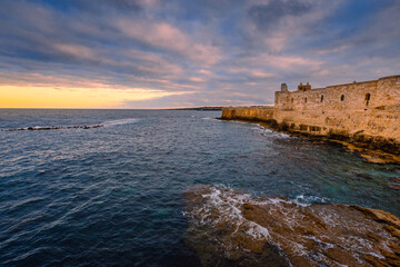 Sunset over the sea with cloudy sky with Maniace Castle in Ortigia