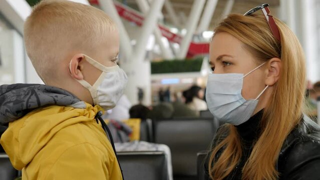A young mother hugs her little son at the airport, they have medical masks on their faces. The family meets at the airport after arrival.