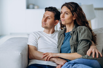 Happy newlyweds with dark hair sit on comfortable sofa in living room and discuss plans for future smiling broadly closeup