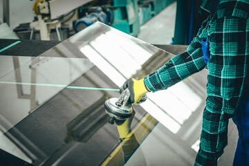 A specialist in a glass company removes a large pane of glass from the table using a specialized...