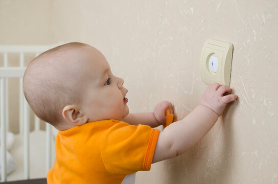 A curious baby touching an electrical outlet. Danger at home for toddlers, safety rules concept.