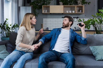 Obraz premium Conflict, quarrel, jealousy in the family home. Young couple, man and woman. The woman is jealous, takes the phone from her husband, demands an explanation