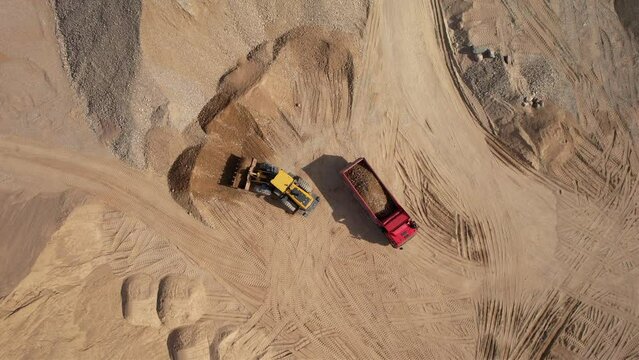 Wheel loader load sand in dump truck in open pit. Heavy machinery on developing opencast. Front end loader on earthworks in quarry. Mining truck transports sand from open-pit mining, drone view.
