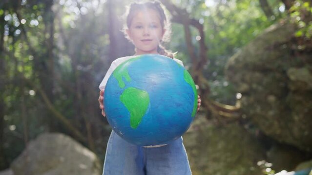 The girl twirls the globe in her hands against the backdrop of nature. plastic pollution in the forest. The concept of World Environment Day, pollution, Global Warming, Earth day.