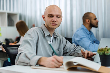 Young bald business man sitting at desk in office, working on computer