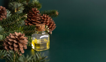 Glass bottle with conifer essential oil near fir branches and pine cones on green close up